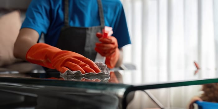 Asian woman cleaning the glass table in the apartment. Cleaning staff maintain cleanliness in with towel and spray detergent.