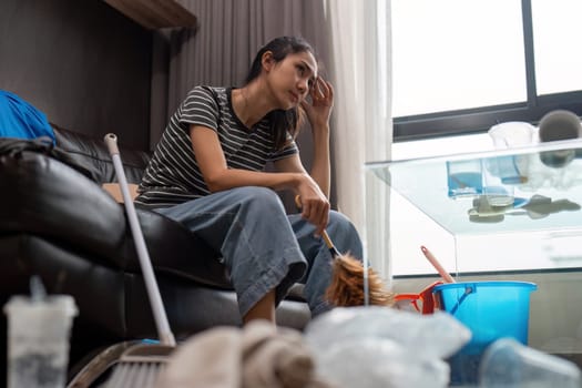 Tired young woman asian in the living room with cleaning products and equipment, housekeeper or overwhelmed girl with housework, stress cleaning, Housework concept.