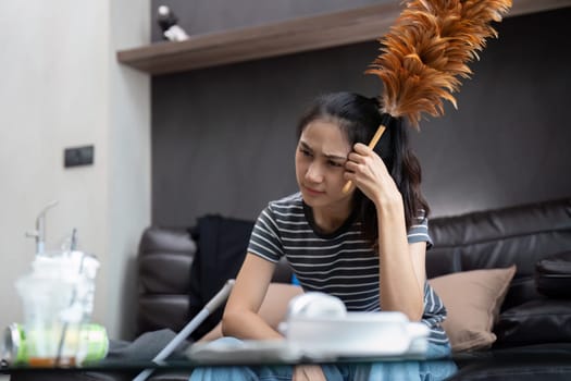 Tired young woman asian in the living room with cleaning products and equipment, housekeeper or overwhelmed girl with housework, stress cleaning, Housework concept.