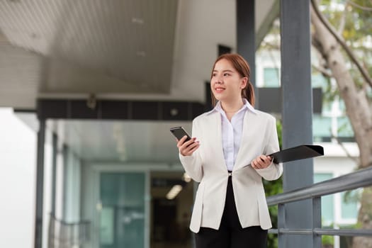 Young Asian business woman entrepreneur, professional manager holding Document file standing on the street in city.