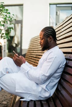 Millennial generation african american man typing sms outdoor 5g internet concept. High speed internet on phone and chatting on social networks and blog