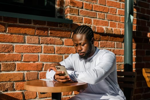 African american man in stylish ethnic dashiki wear viewing photos in social networks on mobile enjoying free time outdoors. Dark-skinned man watching funny video on smartphone and social networks. Blog and blogger scrolling content in Internet.