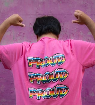 Rear view of gay asian man wearing a pink shirt that says Proud, embracing and supporting LGBTQ community.