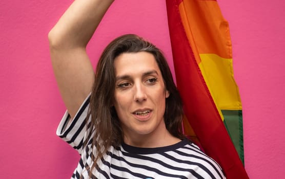 Headshot of a happy transgender woman holding a rainbow flag isolated on pin background.