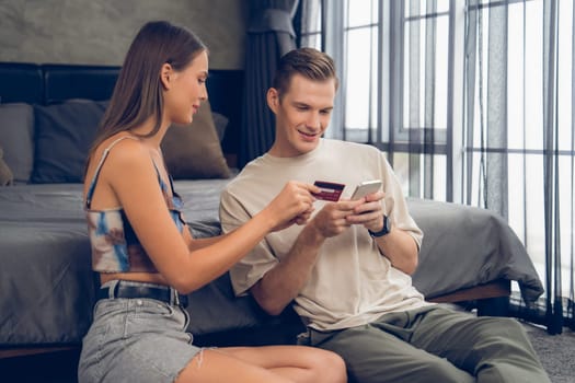 Young couple sit in the home bedroom using online payment app and digital wallet on smartphone to pay with credit card. E commerce shopping and modern purchasing via mobile internet. Unveiling