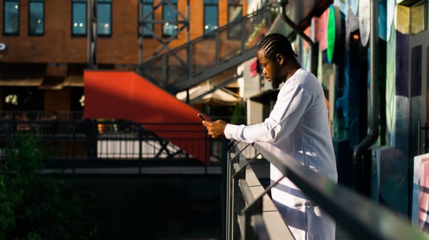 Millennial generation african american man typing sms outdoor 5g internet concept. High speed internet on phone and chatting on social networks and blog