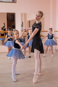 Children's ballet school. Caucasian woman teaching ballet to little girls. Vertical photo