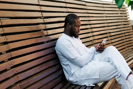 Millennial generation african american man typing sms outdoor 5g internet concept. High speed internet on phone and chatting on social networks and blog