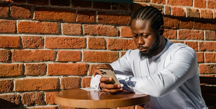 Millennial generation african american man typing sms outdoor 5g internet concept. High speed internet on phone and chatting on social networks and blog