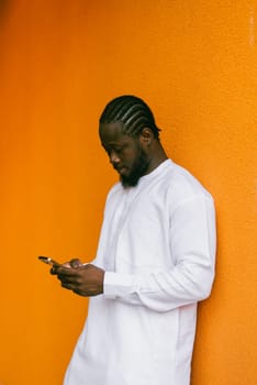 African American hipster guy in cultural and ethnic clothing dashiki chatting on smartphone outdoors, texting with friends on social networks. Millennial and Internet concept.