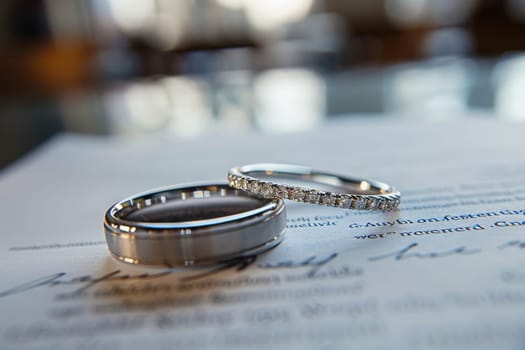 A couple's wedding rings are displayed on a piece of paper. The rings are made of silver and have diamonds on them. The paper is white and has a signature at the bottom