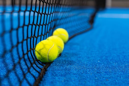 several balls by the net on a blue paddle tennis court. High quality photo