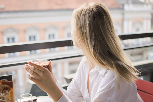 Gen z blonde woman drinks hot chocolate in summer cafe. Tasty beverage and break