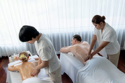 Caucasian couple customer enjoying relaxing anti-stress spa massage and pampering with beauty skin recreation leisure in day light ambient salon spa at luxury resort or hotel. Quiescent