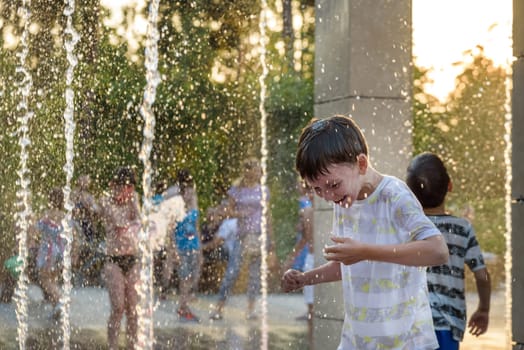 Boys jumping in water fountains. Children playing with a city fountain on hot summer day. Happy friends having fun in fountain. Summer weather. Friendship, lifestyle and vacation.
