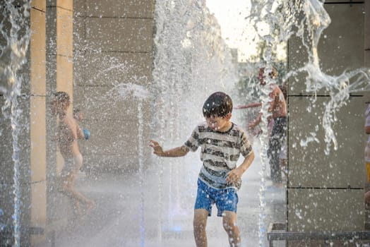 Boy having fun in water fountains. Child playing with a city fountain on hot summer day. Happy kids having fun in fountain. Summer weather. Active leisure, lifestyle and vacation.