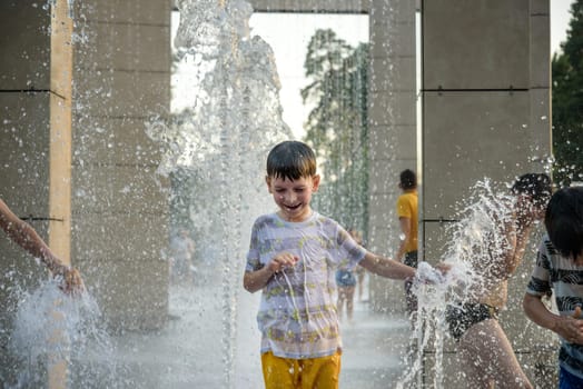 Boy having fun in water fountains. Child playing with a city fountain on hot summer day. Happy kids having fun in fountain. Summer weather. Active leisure, lifestyle and vacation.