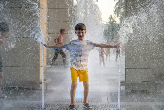 Boy having fun in water fountains. Child playing with a city fountain on hot summer day. Happy kids having fun in fountain. Summer weather. Active leisure, lifestyle and vacation.