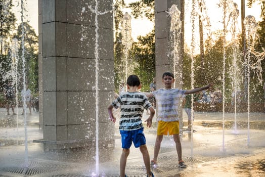 Boys jumping in water fountains. Children playing with a city fountain on hot summer day. Happy friends having fun in fountain. Summer weather. Friendship, lifestyle and vacation.