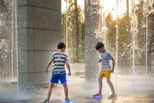 Boys jumping in water fountains. Children playing with a city fountain on hot summer day. Happy friends having fun in fountain. Summer weather. Friendship, lifestyle and vacation.