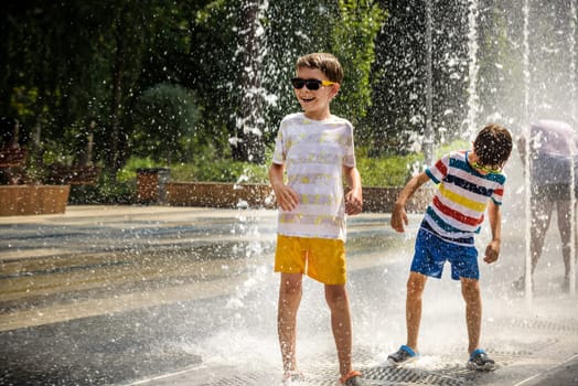 Boy having fun in water fountains. Child playing with a city fountain on hot summer day. Happy kids having fun in fountain. Summer weather. Active leisure, lifestyle and vacation.