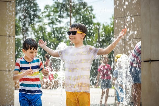 Boy having fun in water fountains. Child playing with a city fountain on hot summer day. Happy kids having fun in fountain. Summer weather. Active leisure, lifestyle and vacation.