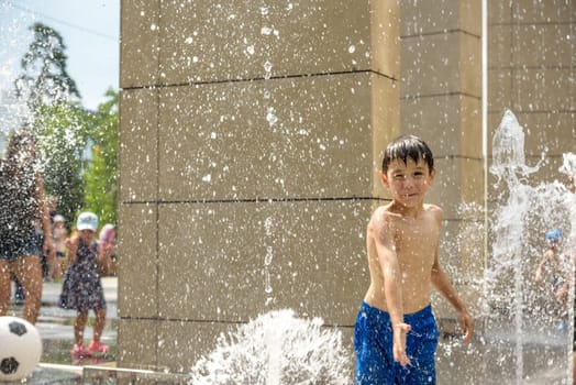 Boy having fun in water fountains. Child playing with a city fountain on hot summer day. Happy kids having fun in fountain. Summer weather. Active leisure, lifestyle and vacation.