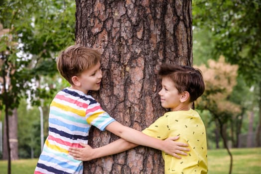 Two Little boys hugs a tree trunk - children love the nature, sustainability concept. Save the nature.