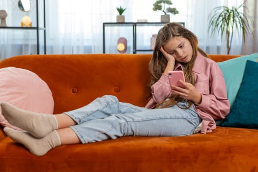 Upset girl using smartphone playing game loses becoming surprised sudden lottery results, bad news, fortune loss, fail education study test. Female teen child kid at home in living room sits on sofa.