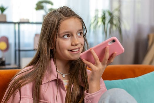 Happy girl child making online phone call conversation with friends. Portrait of Caucasian female teenager enjoying mobile loudspeaker talking chatting communication at home living room on couch.