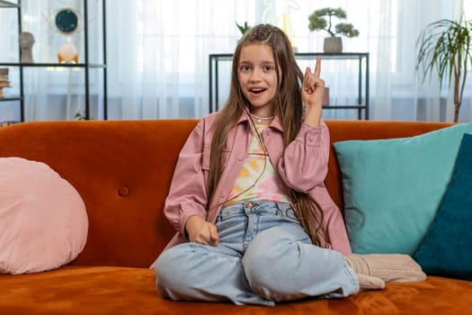 Eureka. Inspired girl pointing finger up having good idea, plan, startup, showing inspiration motivation gesture, problem solution. Young stylish child kid sitting on sofa couch in living room at home