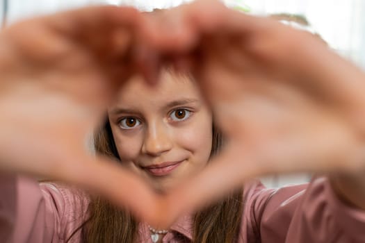 I love you. Caucasian child kid girl makes symbol of love, showing heart sign to camera, express romantic feelings, express sincere positive feelings. Charity, gratitude, donation. Female teen at home