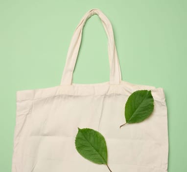 Empty beige textile bag on green background, rejection of plastic bags, flat lay, zero waste 