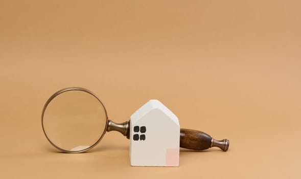Wooden house and a magnifying glass, representing the concept of real estate purchase, rental growth, and mortgage interest