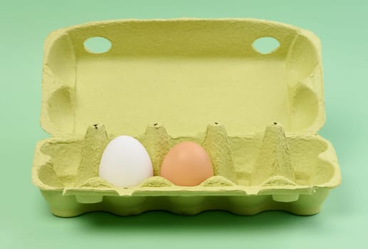 Two chicken eggs in a paper box on a green background