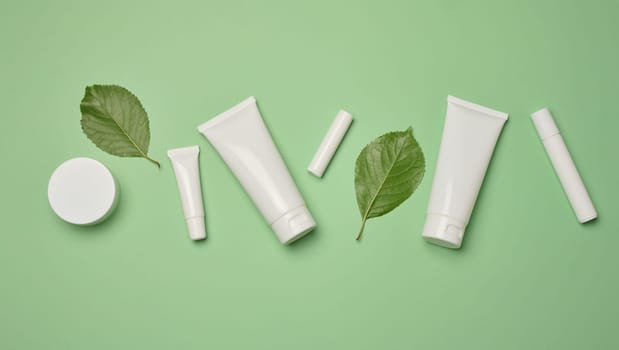 White plastic tubes, jars, and containers for cosmetic products on a green background, advertising and branding of products