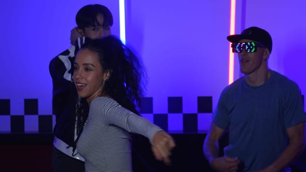 Diverse people in casual shirt with fancy glasses dancing with neon light. Multicultural break dancer looking at camera and perform street dancing while dancing together at night club. Regalement.