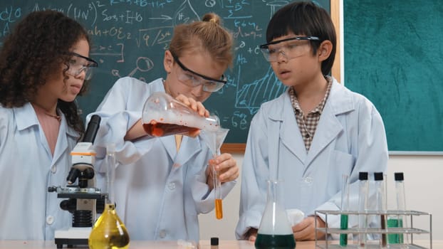 Caucasian student doing experiment and pouring biochemical solution surrounded by curious children waiting for discover new innovation at laboratory. Diverse happy student doing experiment. Pedagogy.