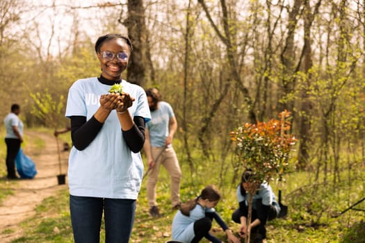 Young teenager activist planting small green seedlings in the woods, restoring natural habitat and protecting the environment. Proud african american girl doing voluntary work to save the planet.