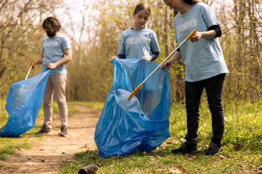 Diverse people collecting rubbish and storing in the trash disposal bag, picking up junk and plastic bottles to help with pollution. Clearing the forest, ecosystem protection.