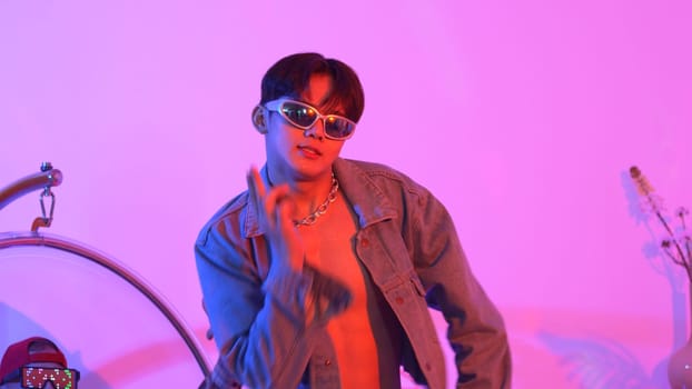 Close up of asian street dancer moving to pop music with neon light while diverse friend sitting and support performance. Professional performer practicing dancing step to beat at studio. Regalement.
