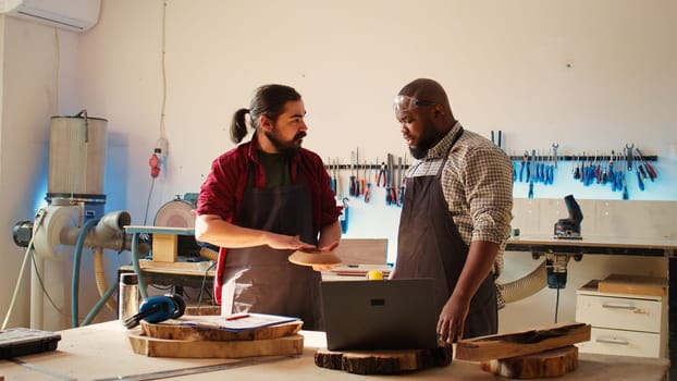 Carpenter and african american coworker verifying finished wood art product before sending it to client. Artisan and apprentice inspecting wooden object to correspond to requirements