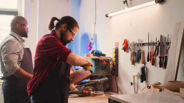 Carpenter doing last touches on piece of wood before using it for furniture assembly, sanding it with sandpaper. Woodworking expert doing woodworking process on lumber block, fixing damages, camera B