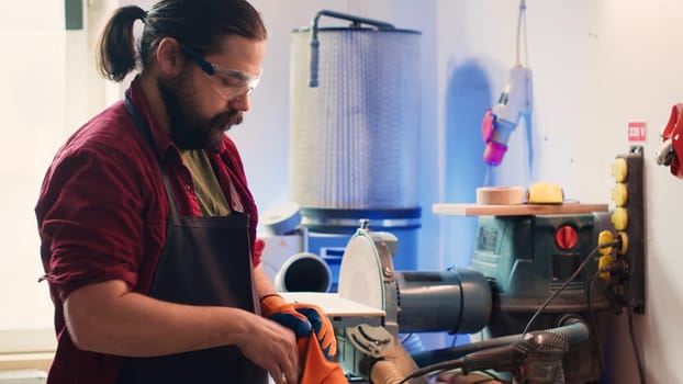 Carpenter in woodworking shop putting on protection gloves before assembling furniture. Cabinetmaker wearing safety equipment before starting work to avoid injuries, camera A