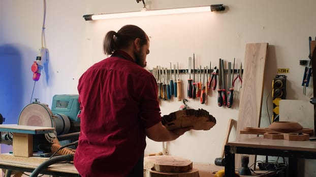 Carpenter selecting tool from rack to use on wood materials, helped by african american coworker. Craftsperson doing quality assurance on lumber pieces pile with BIPOC apprentice, camera A