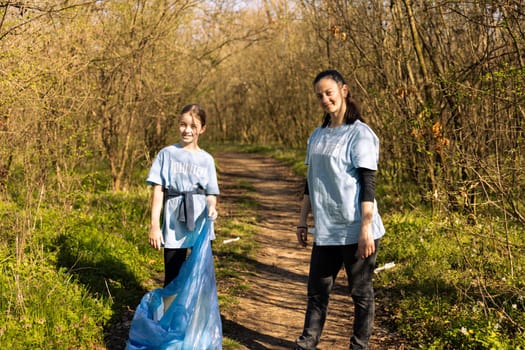 Proud mother and daughter volunteering to fight pollution, restoring natural environment and helping with illegal dumping. Little kid recycling plastic waste in a disposal bag.