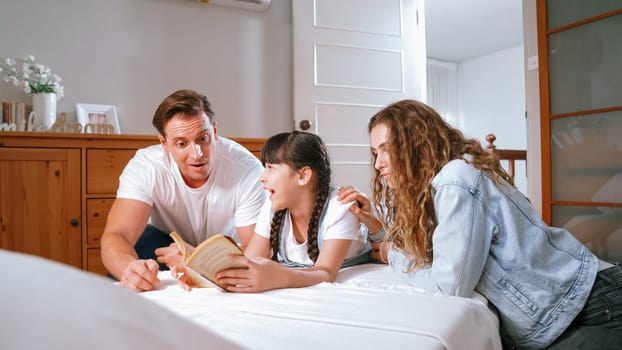 Bedtime story with childhood storytelling, mom and dad reading a fantasy book together to their little young girl in cozy and comfortable bedroom. Modern family happy time. Synchronos