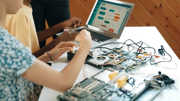 Top view of diverse children working together coding program. while caucasian teacher check and inspect system. Young children using electronic tool to fix motherboard at STEM class. Edification.