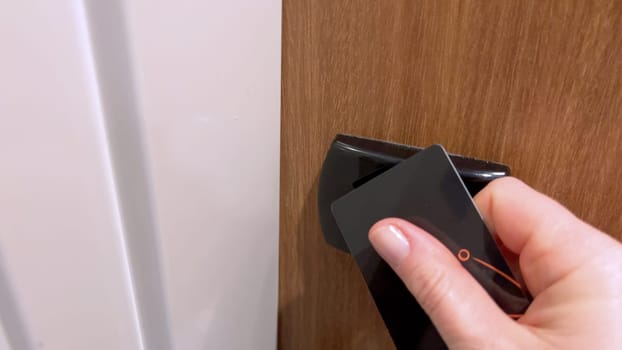 Close-up view of a guest hand using a black key card to unlock a hotel room door, demonstrating the security and convenience of modern hotel access systems.