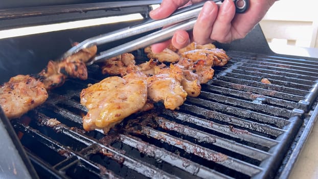 A close-up image capturing the process of grilling marinated chicken pieces, with a person expertly flipping them to ensure even cooking on a classic outdoor barbecue grill.